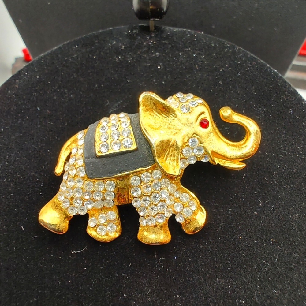 Adorable gold tone elephant encrusted with rhinestones and a red rhinestone eye.